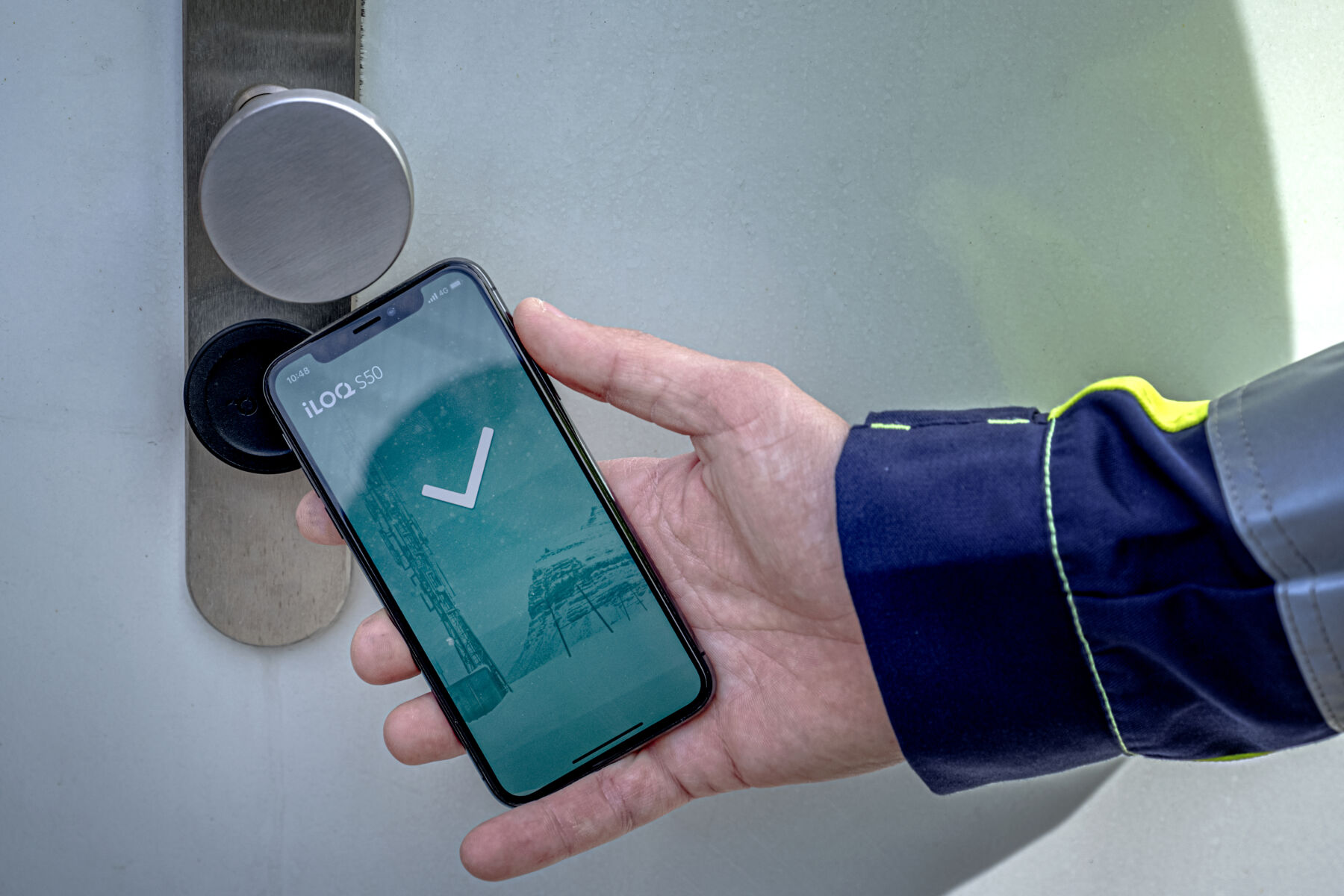 Ein Smartphone wird zur Türöffnung über eine App genutzt. Das Smartphone wird dazu vor den Türbeschlag gehalten.